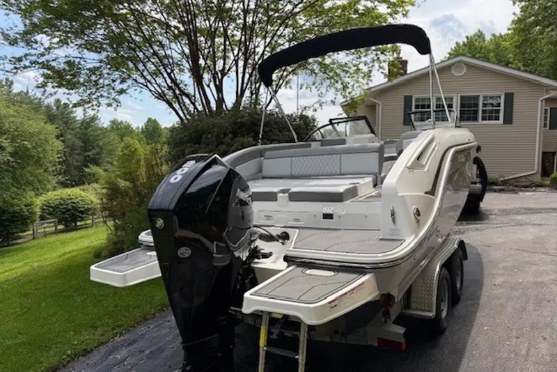 Slide: The Image of 2023 Bayliner DX 2200 boat on trailer, parked in a driveway near a house. - 2