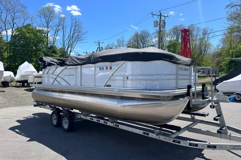 Slide: The Image of 2024 Sylvan Mirage 8522 LZ pontoon boat on trailer, parked outdoors under clear sky. - 25