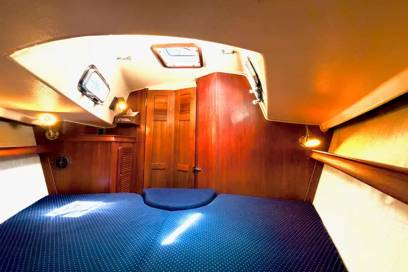 Slide: The Image of Cozy cabin interior of a 1992 Island Packet 29 sailboat with wooden accents and blue bedding. - 37