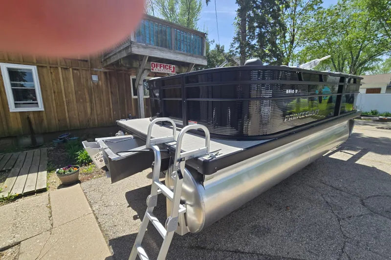 Slide: The Image of 2026 Princecraft Brio 17 Electric pontoon boat parked near a rustic wooden building. - 4