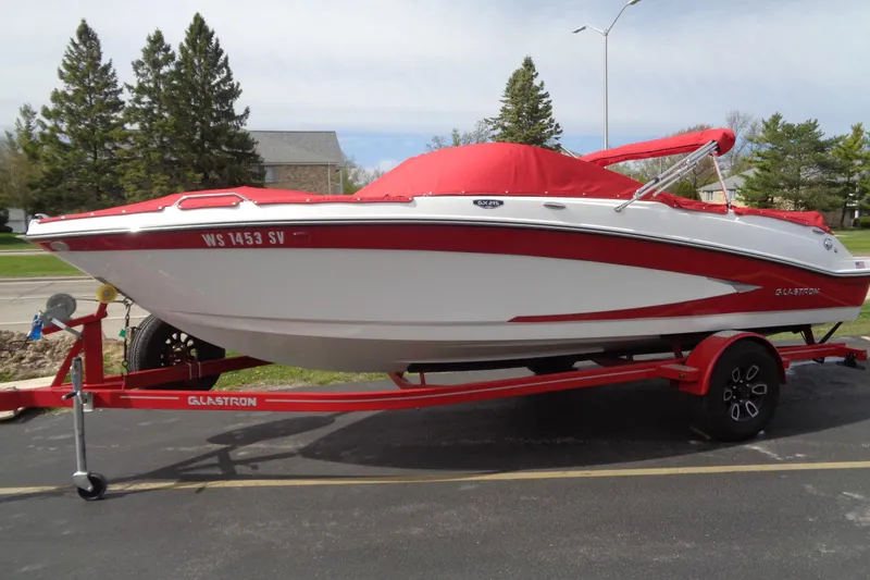 The Image of 2022 Glastron GX 215 boat with red cover on a matching trailer, parked outdoors. - 0