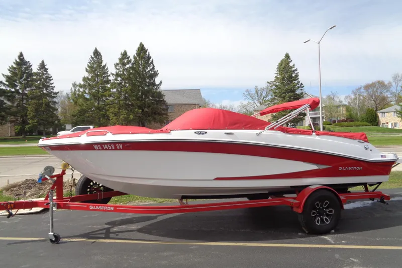 Slide: The Image of 2022 Glastron GX 215 boat with red cover on a matching trailer, parked outdoors. - 1