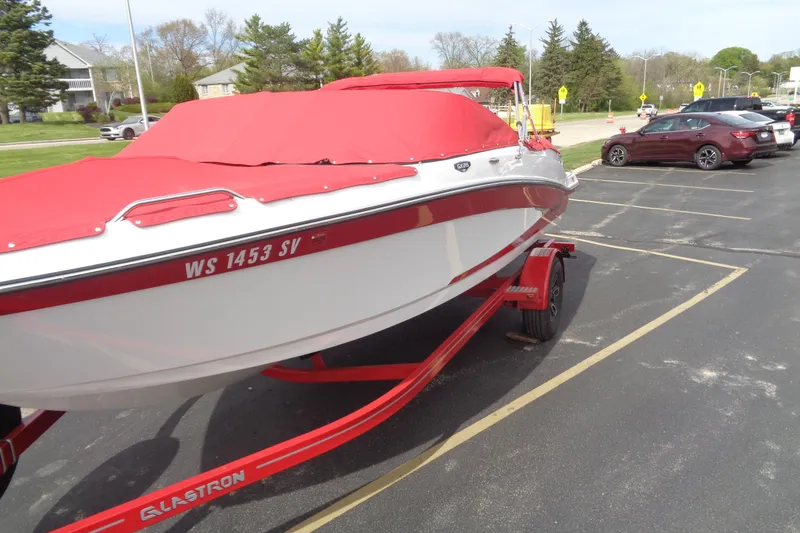 Slide: The Image of 2022 Glastron GX 215 boat with red cover on a trailer in parking lot. - 2