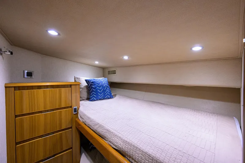 Slide: The Image of 2015 Viking 52 Open yacht cabin with bed, wooden dresser, and ambient lighting. - 66
