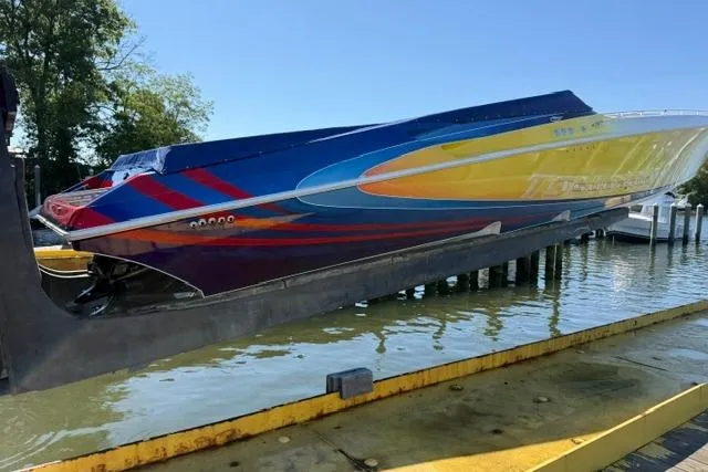 Slide: The Image of 2000 Fountain 47 Lightning speedboat with vibrant colors on a lift by the water. - 2