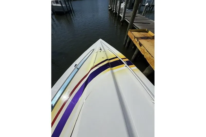 Slide: The Image of Bow view of a 2000 Fountain 47 Lightning boat docked, featuring colorful stripes. - 29