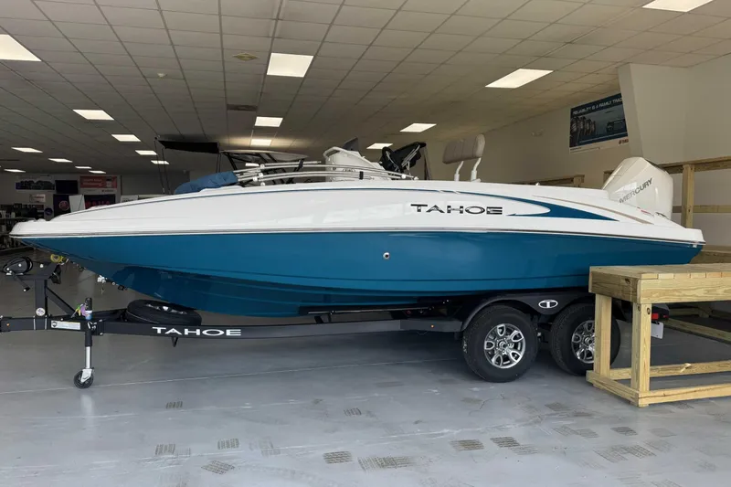 The Image of 2026 Tahoe 2150 CC boat in showroom, featuring sleek blue and white design on trailer. - 0