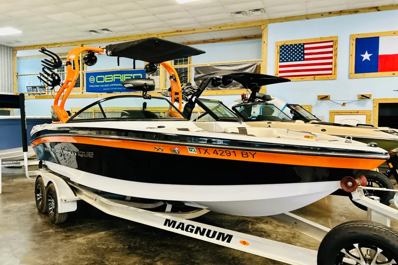 Slide: The Image of 2013 Nautique Super Air Nautique 230 boat on trailer in showroom with flags displayed. - 12