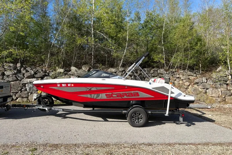 The Image of 2023 Scarab 215 ID boat on trailer, red and white design, parked outdoors. - 0