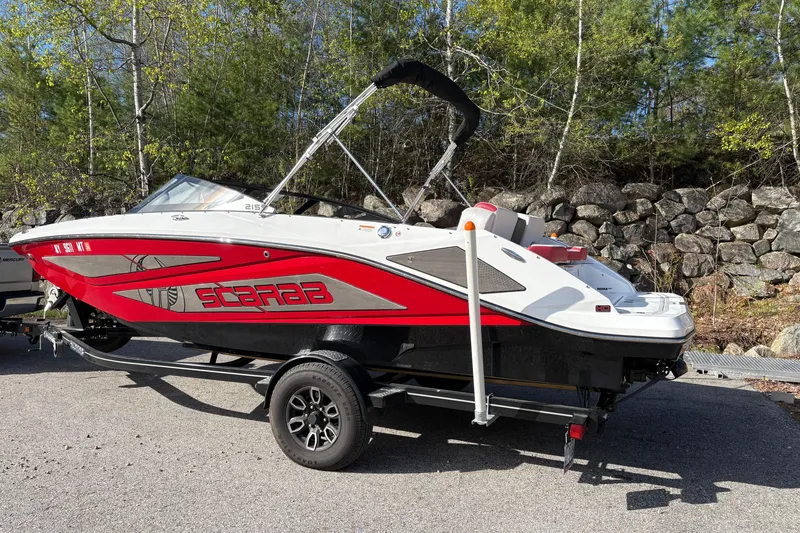 Slide: The Image of 2023 Scarab 215 ID boat on trailer, red and white design, parked outdoors. - 2