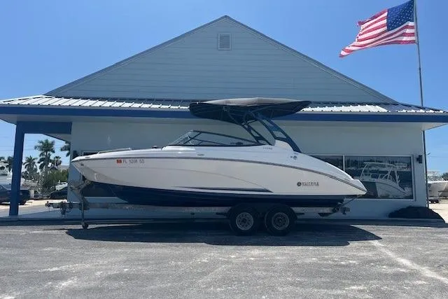 The Image of 2022 Yamaha 242SE boat on trailer, parked outside building with American flag. - 1