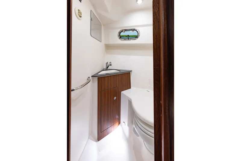 Slide: The Image of 2026 Pursuit OS 325 Offshore boat bathroom with sink, toilet, and porthole window. - 19