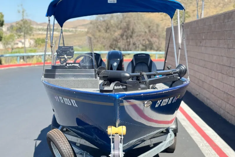 Slide: The Image of 2025 Lund 1650 Angler SS boat with blue canopy, parked on a trailer. - 2