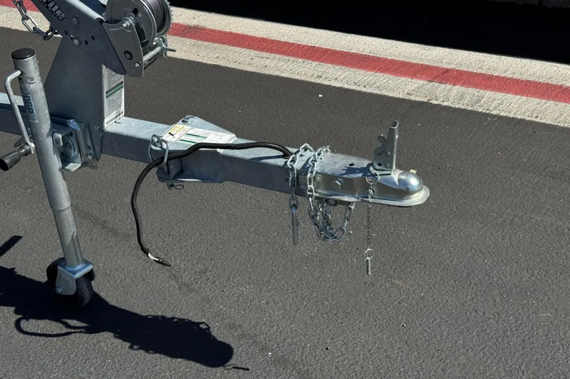 Slide: The Image of Trailer hitch of a 2025 Lund 1650 Angler SS on asphalt, featuring chains and a winch. - 22