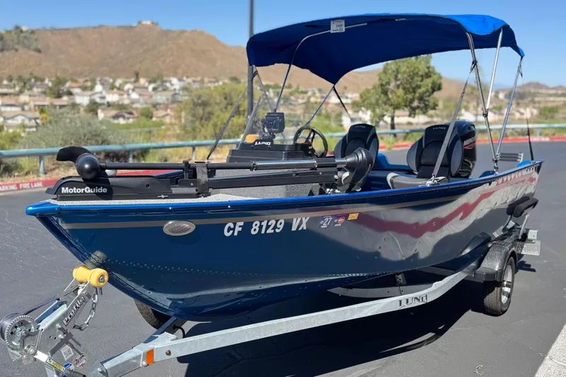 Slide: The Image of 2025 Lund 1650 Angler SS boat with blue canopy on trailer, parked outdoors. - 3
