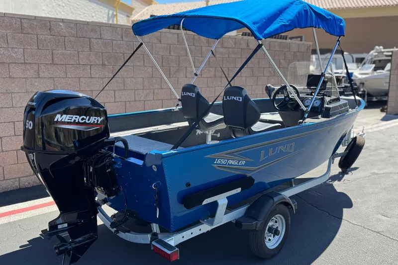 Slide: The Image of 2025 Lund 1650 Angler SS boat with Mercury engine, blue canopy, parked on trailer. - 5