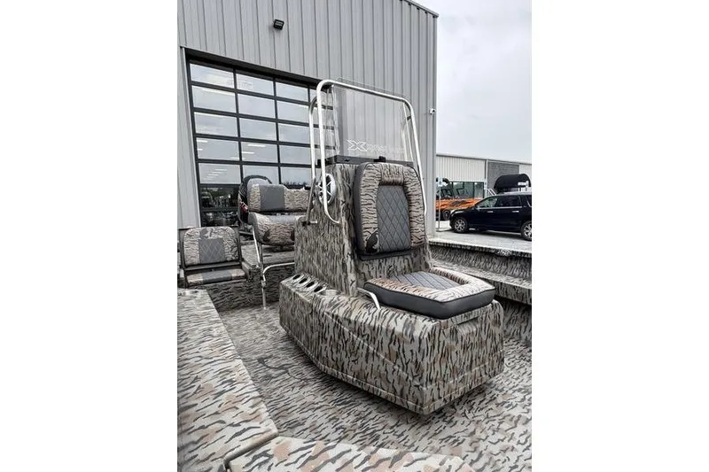 Slide: The Image of 2026 Xpress H22B Bay boat with camouflage seating, parked outside a modern building. - 18