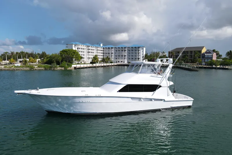 The Image of 2004 Hatteras 60 Convertible yacht cruising in a scenic marina with buildings in the background. - 0