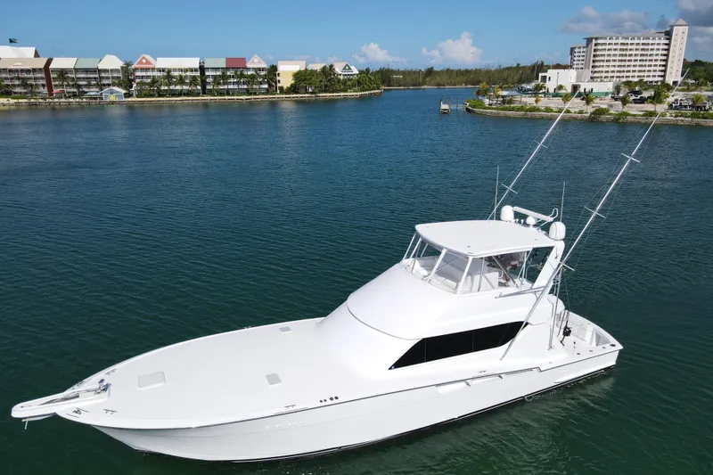 Slide: The Image of 2004 Hatteras 60 Convertible yacht on calm water, with scenic waterfront background. - 15