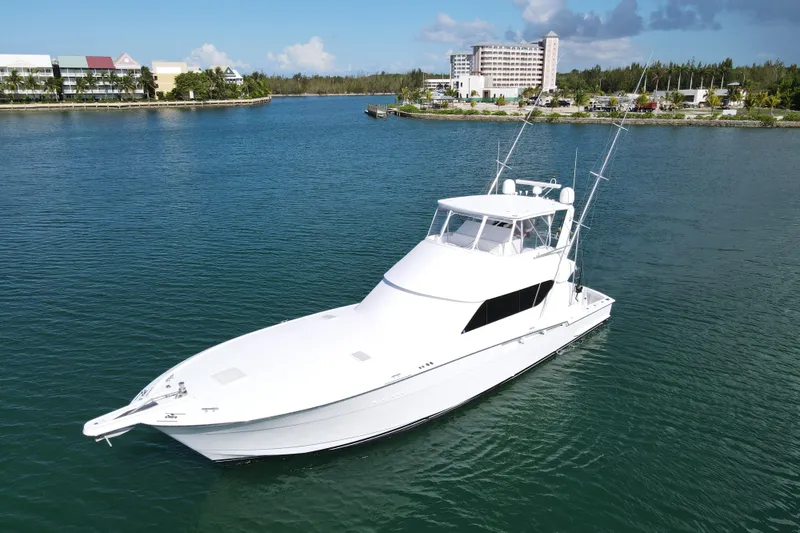 Slide: The Image of 2004 Hatteras 60 Convertible yacht on calm water near a coastal resort. - 17