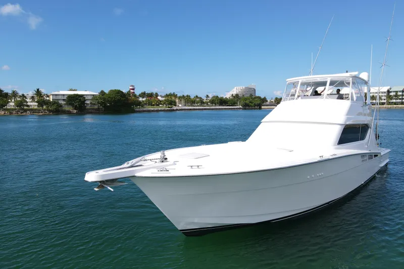 Slide: The Image of 2004 Hatteras 60 Convertible yacht cruising on clear blue waters near a scenic shoreline. - 19