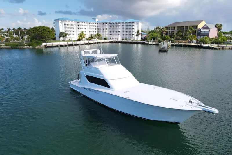 Slide: The Image of 2004 Hatteras 60 Convertible yacht on calm water near a coastal building. - 28