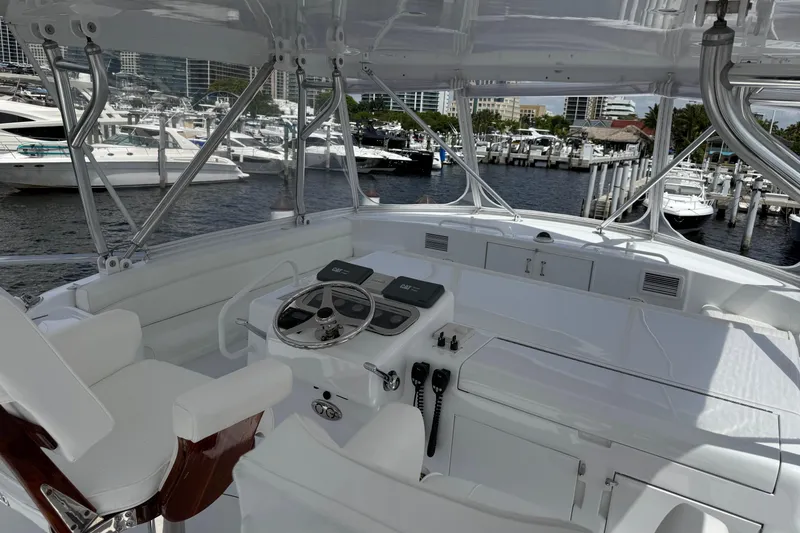 Slide: The Image of 2004 Hatteras 60 Convertible yacht helm with marina view, featuring sleek white design and modern controls. - 47