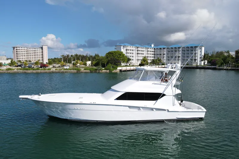 Slide: The Image of 2004 Hatteras 60 Convertible yacht cruising near waterfront buildings under cloudy sky. - 6
