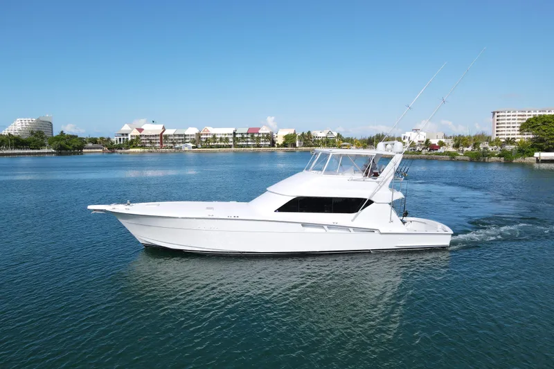 Slide: The Image of 2004 Hatteras 60 Convertible yacht cruising on calm waters near a coastal cityscape. - 7