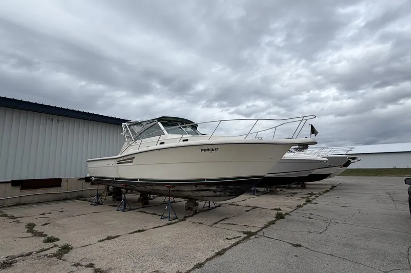 Slide: The Image of 1998 Pursuit 3400 Express boat on stands, overcast sky background. - 3
