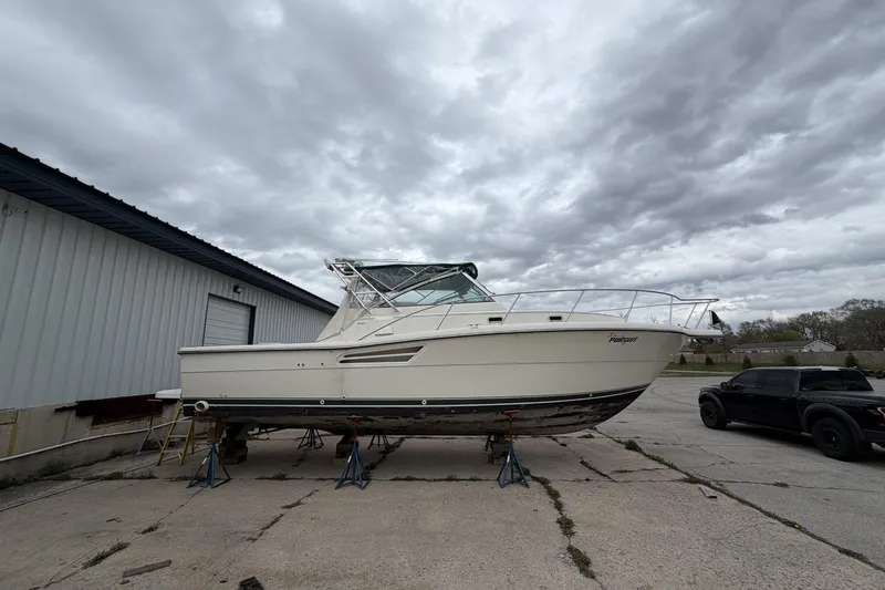 Slide: The Image of 1998 Pursuit 3400 Express boat on stands, overcast sky, parked near a building. - 5