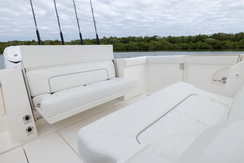 Slide: The Image of 2026 Pursuit S 328 Sport boat interior with white seating and fishing rods, near lush shoreline. - 3