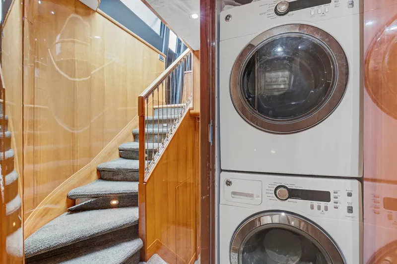 Slide: The Image of Laundry area with stacked washer and dryer beside a carpeted staircase on a 2004 Queenship 76 Baretta yacht. - 23