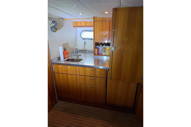 Slide: The Image of Wooden yacht kitchen interior with sink, storage cabinets, and porthole window on a 2004 Queenship 76 Baretta. - 71