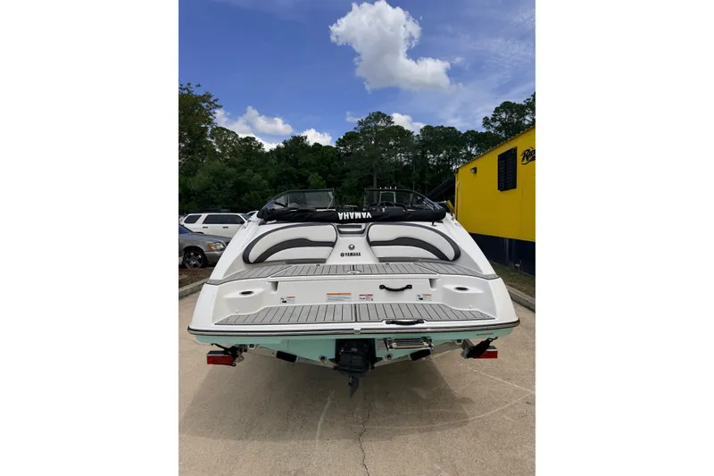 Slide: The Image of 2026 Yamaha Boats SX195, rear view, parked outdoors with trees and a yellow building. - 4