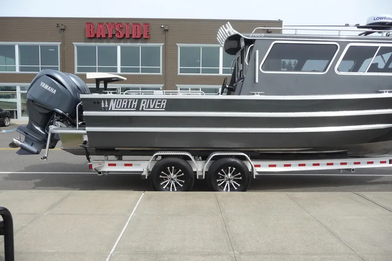 Slide: The Image of 2025 North River 2700s boat on trailer, parked outside Bayside building. - 3