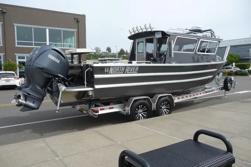 Slide: The Image of 2025 North River 2700s boat on trailer with Yamaha engine, parked near modern building. - 6