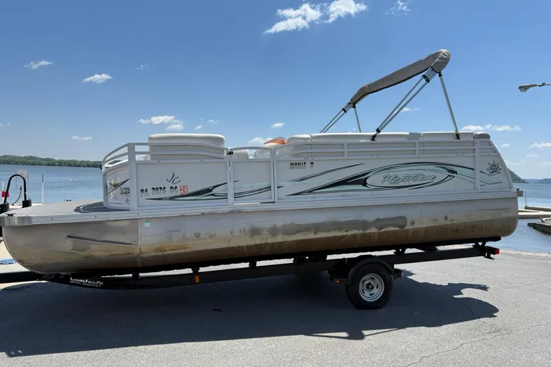 The Image of 2010 JC 21 Neptoon pontoon boat on trailer by a lake under clear blue sky. - 1