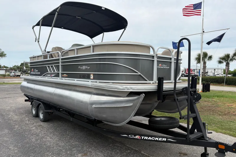 Slide: The Image of 2023 Sun Tracker Party Barge 22 DLX pontoon boat on trailer, parked near flags. - 5