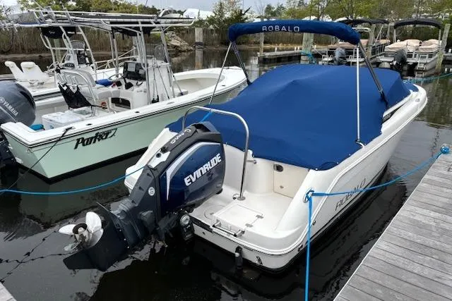 Slide: The Image of 2017 Robalo R227 Dual Console boat with blue cover docked beside another vessel. - 4