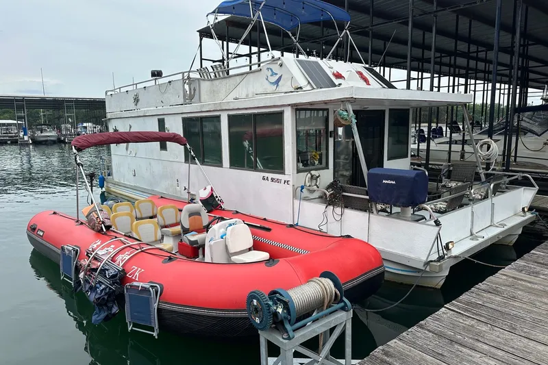 The Image of 1996 Catamaran Cruisers 12x42 houseboat docked with red inflatable boat. - 0