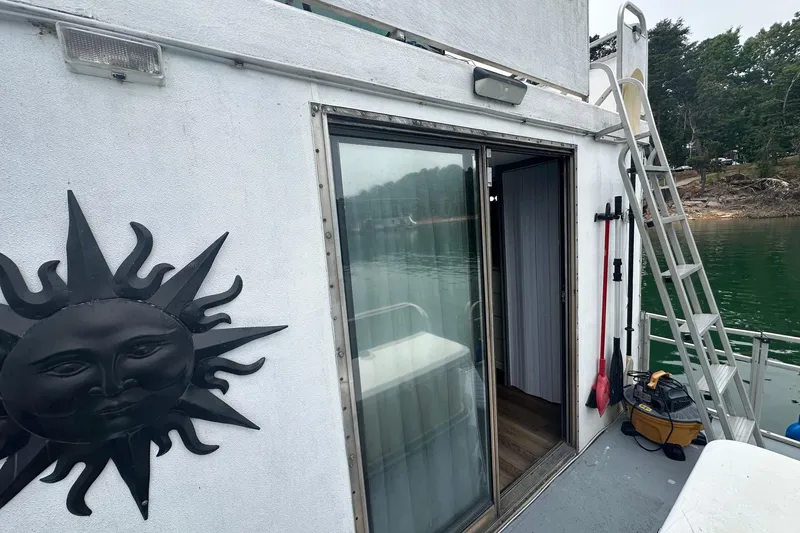 Slide: The Image of 1996 Catamaran Cruisers 12x42 houseboat with sun decoration, sliding door, and ladder by the water. - 13