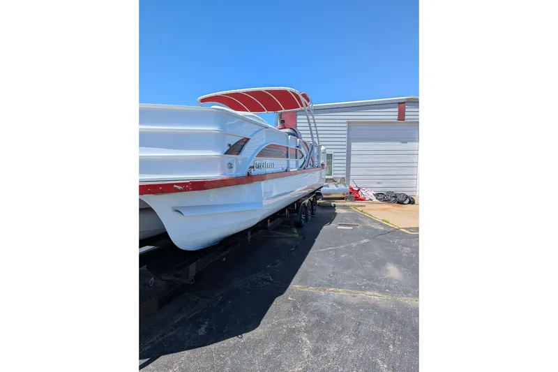 Slide: The Image of 2025 PlayCraft 3000 XTREME pontoon boat with red canopy, parked outdoors. - 2