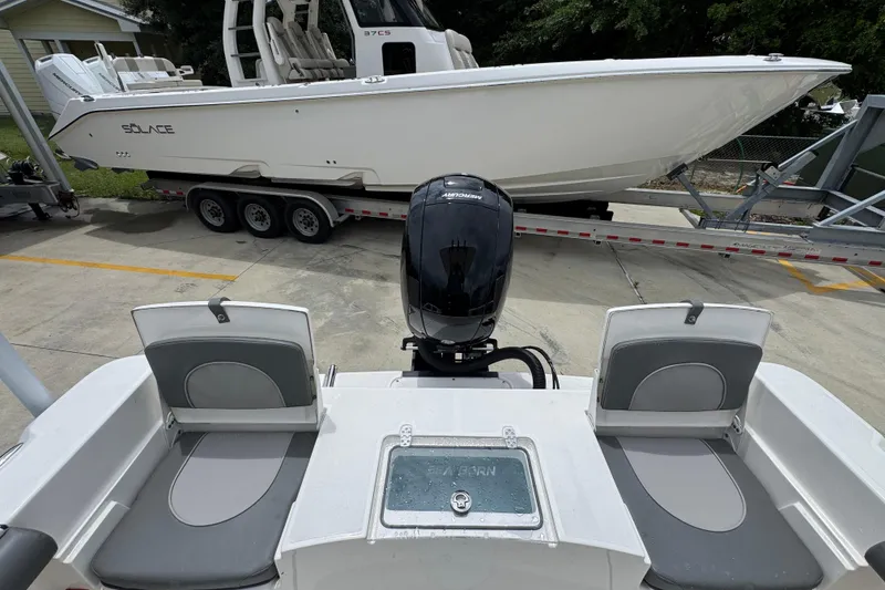 Slide: The Image of 2026 Sea Born LX21 Center Console boat with outboard motor, parked near a larger vessel. - 29