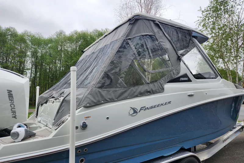 Slide: The Image of 2022 Finseeker 280 DC boat with canopy, parked on trailer, surrounded by trees. - 11