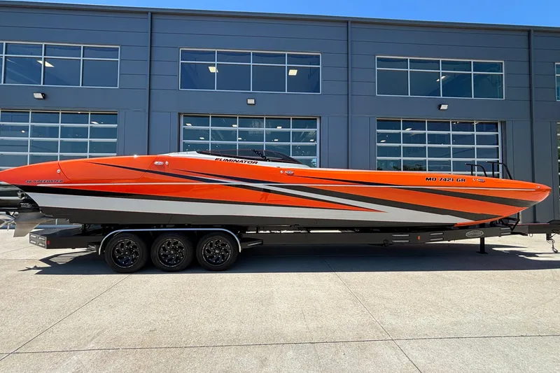 The Image of 2020 Eliminator 36 Daytona Coupe boat, vibrant orange design, parked on a trailer outside a modern building. - 1