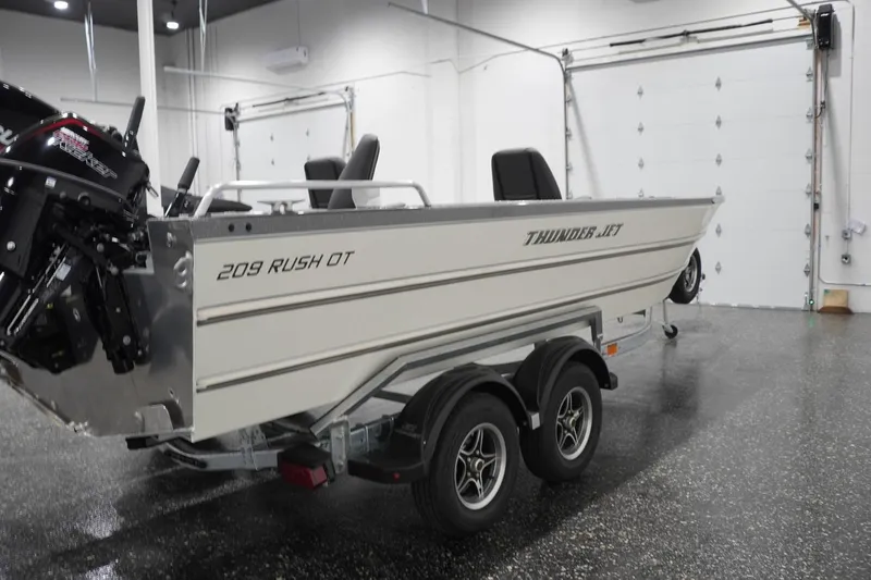 Slide: The Image of 2026 Thunder Jet 209 Rush OT boat in showroom, featuring dual-axle trailer and powerful outboard motor. - 12