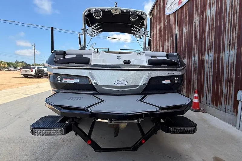 Slide: The Image of 2019 MasterCraft X22 boat, rear view, parked beside a rustic building. - 2