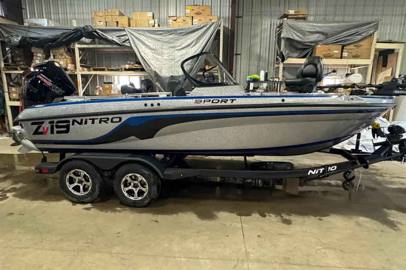 The Image of 2026 Nitro ZV19 Sport Pro boat in a warehouse, showcasing sleek design and dual-axle trailer. - 0