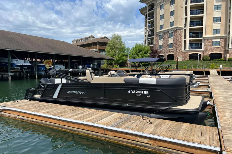 The Image of 2026 Starcraft SLS 3 R pontoon boat docked at a marina with modern buildings. - 0